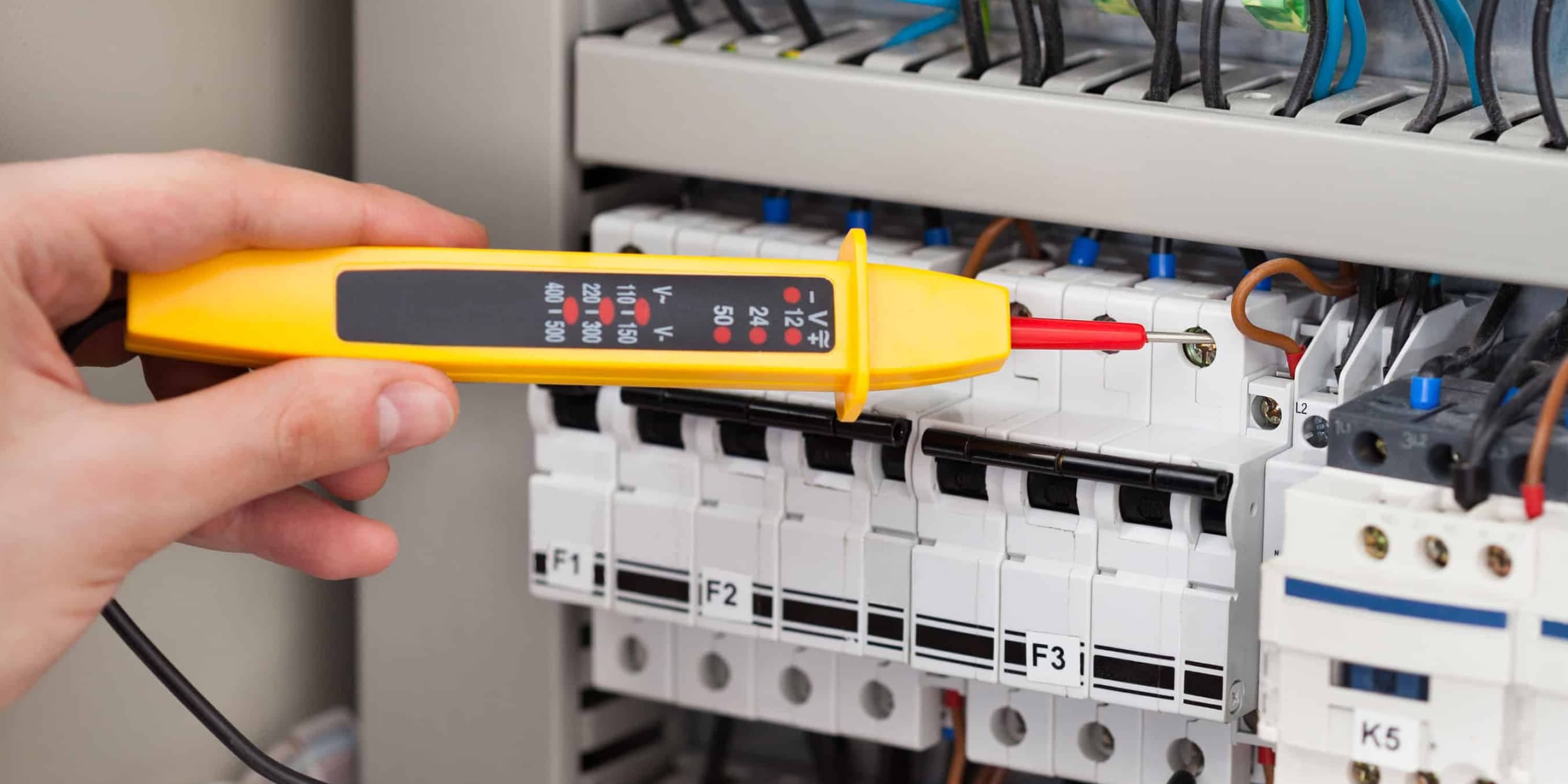 Main d'un électricien utilisant un testeur de tension jaune sur des disjoncteurs électriques.